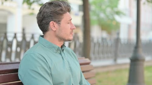 Man Sitting Thoughtfully on Bench in Urban Park
