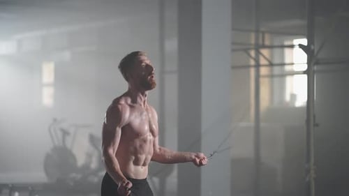 A Young Athletic Man with Prominent Muscles Jumps on a Rope in the Gym in Slow Motion
