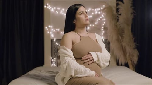 Cheerful Pregnant Woman Sitting on Bed and Touching Belly