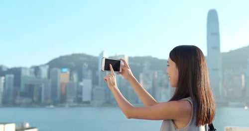 Woman taking photo with cellphone on Victoria harbor in Hong Kong