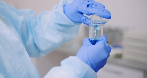 Person Mixing Blue Liquid in Laboratory Beakers