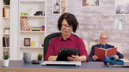 Woman Using Tablet While Man Reads Book at Home