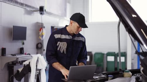 Portrait of Mechanic Uses a Laptop While Conducting Diagnostics Test on Engine