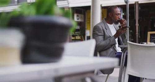 Man Using Phone and Drinking Coffee at Cafe