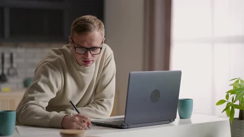 Man Working from Home on Laptop and Writing Notes