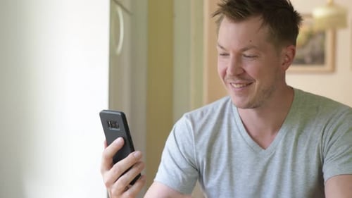 Smiling Man Uses Smartphone Indoors