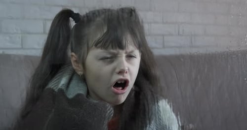 Shivering Child Wrapped in Blanket by Rainy Window