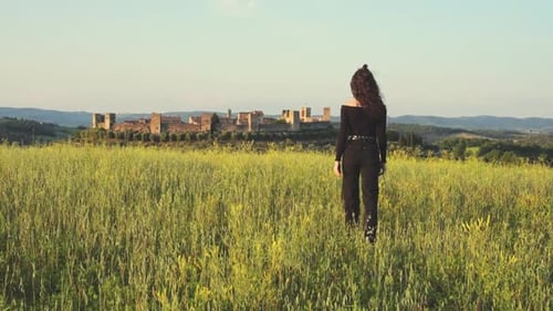 Woman Walks Through Field Towards Distant Castle