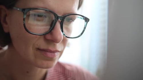 Rosto de uma mulher com óculos olhando para a tela do monitor do computador.