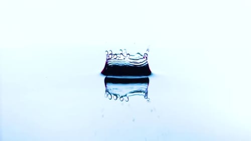 A Transparent Drop of Water Falls on the Surface of a Pink Liquid in Slow Motion.