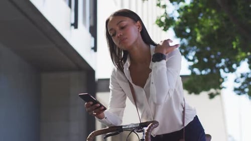 African american woman using smartphone leaning on bike in street