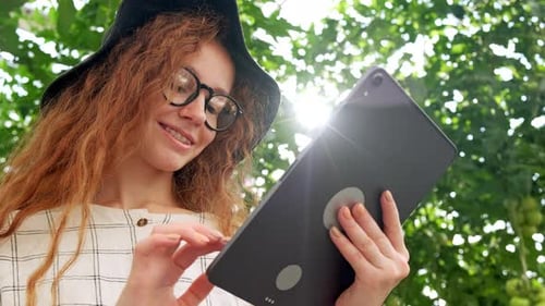 Young Woman Using or Playing Tablet in Greenhouse. Green Plant Growing in Warm House.