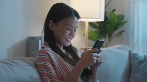 Asiatische schöne Frau sitzt auf dem Sofa und unterhält sich nachts mit dem Handy.