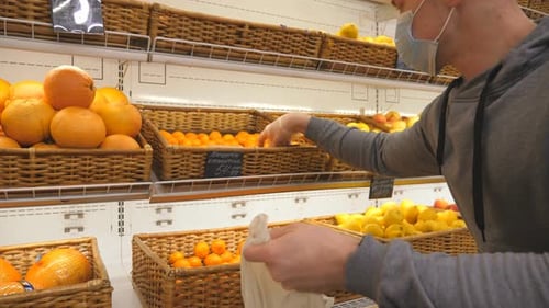 Man with Medical Face Mask Selects Mandarins in Store. Guy Choose Fruits in Supermarket. Purchase