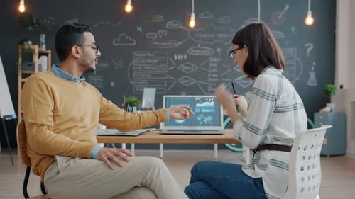 Cheerful Coworkers Arab Man and Caucasian Girl Talking Using Laptop in Office