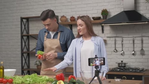 Jeune couple cuisinant ensemble et enregistrant un blog vidéo sur la nourriture devant la caméra dans la cuisine à la maison