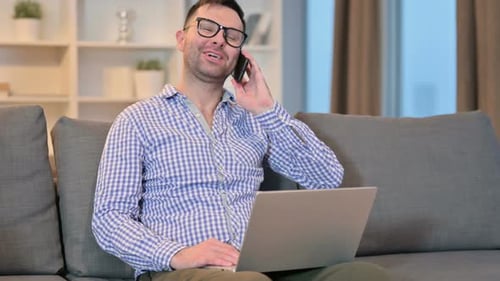 Man Talking on Phone While Using Laptop at Home