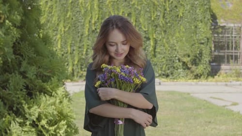 Portrait of Pretty Smiling Young Woman Holding Bouquet of Wild Flowers Looking at Camera