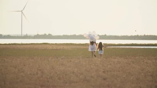 Woman and Child Walking With Balloons in Field