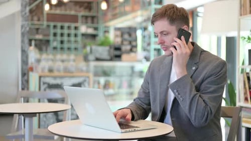 Young Adult Working on Laptop and Phone in Cafe