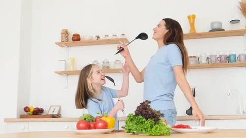 Cheerful Mother and Daughter Dancing and Singing in Kitchen