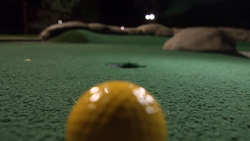 A compilation of a yellow mini golf ball falling into the golf hole and bounces in the pocket on a c