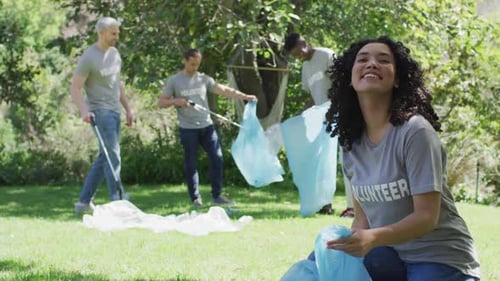 Happy diverse group of friends in volunteer t shirts putting plastic waste in refuse sacks outdoors