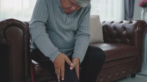 Senior Massaging Leg on Couch Indoors