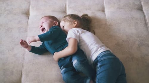 Girl Hugs Crying Infant on Couch