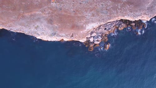 Vista aérea de arriba hacia abajo de las olas chapoteando contra la costa rocosa, fondo. Vuelo sobre altos acantilados de