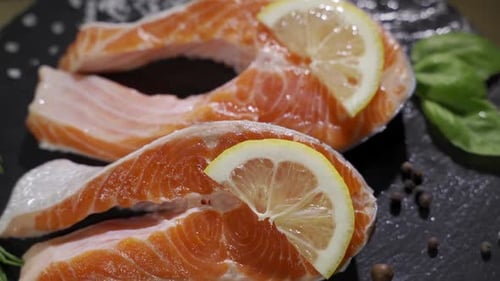 Lachs. Rotes Forellen-Fischsteak mit Kräutern und Zitrone und Olivenöl, rotiert auf Schiefer. Zeitlupe