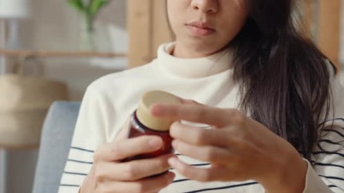 Woman Taking Pills From Amber Bottle At Home