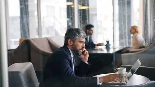 Entrepreneur in Talking on Mobile Phone and Using Laptop Working in Cafe