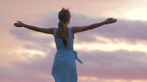 Dark Silhouette of a Young Woman Standing with Raised Up Hands on a Stone Enjoying Sunset View