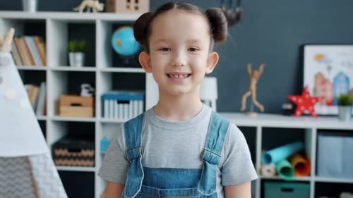 Smiling Girl in Overalls Standing Indoors at Home