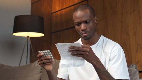 Black Man Reads the Instructions for Medicinal Pills and Side Effects While Sitting on the Couch