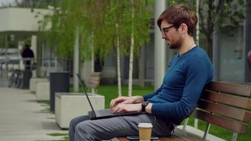 Young business man using laptop while sitting outdoor city park.