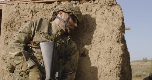 Injured Soldier in Camouflage Leaning Against Mud Wall