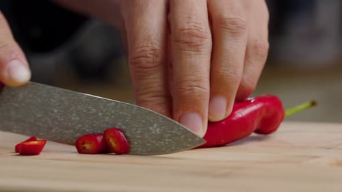 Person Slices Red Chili Pepper on Cutting Board