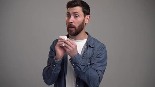 Man Sneezes and Wipes Nose with Tissue