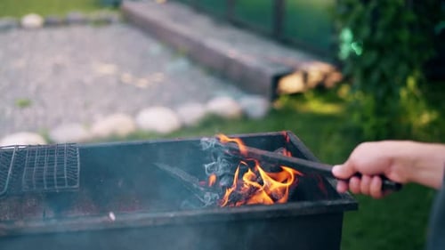 Close-up: Man Prepares the Coals in the Grill, Stirs Them with a Stick.