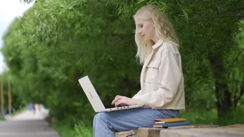 Young Blonde Woman Works for a Laptop in the Park