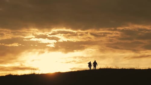 Silhouettes of Two Hikers with Backpacks Enjoying Sunset View From Top of a Mountain. Enjoying the