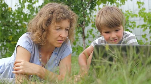 Woman and Child Watching Tablet in Grass