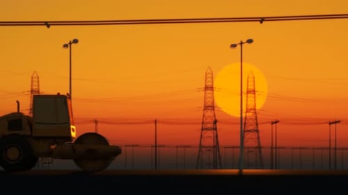 Road roller moving left to right paving asphalt road. Sunset over urban area.
