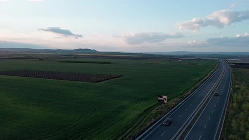 Road with Cars and Trucks on It Passes Through Fields Under a Colored Sky