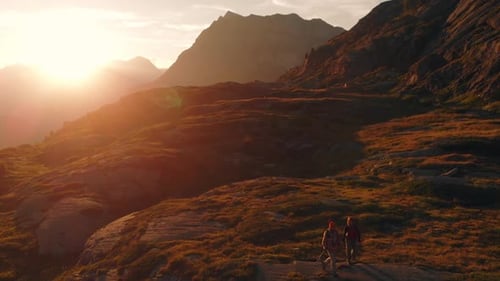 Aerial: couple backpackers hiking to the mountain top, rocky mountain peak in backlight