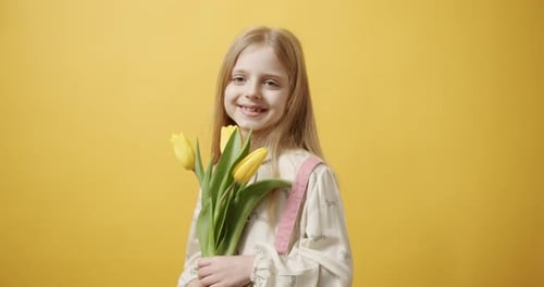 Smiling Girl Holding Yellow Tulips in Front of Yellow