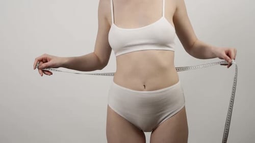 Slim Woman Measuring Her Waist's Size with Tape Measure on White Background