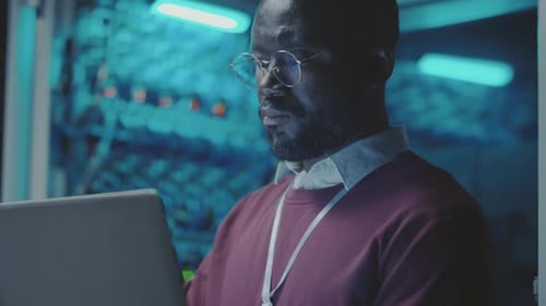 Focused Man Working on Laptop in Server Room